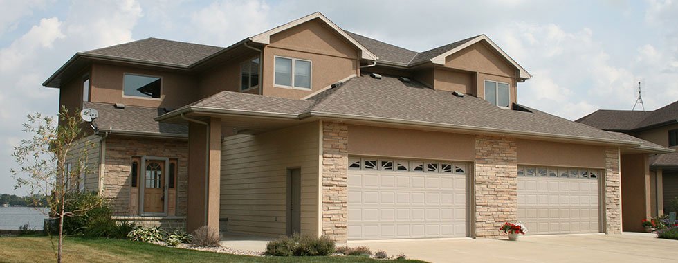 Front of tan suburban home with two car garage and green lawn